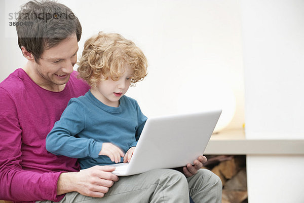 Nahaufnahme eines Mannes,  der seinem Sohn bei der Benutzung eines Laptops hilft.