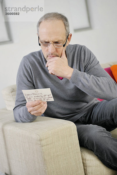 Mann,  der beim Lesen einer Postkarte ernsthaft aussieht