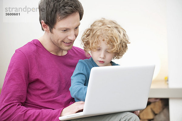 Nahaufnahme eines Mannes,  der seinem Sohn bei der Benutzung eines Laptops hilft.