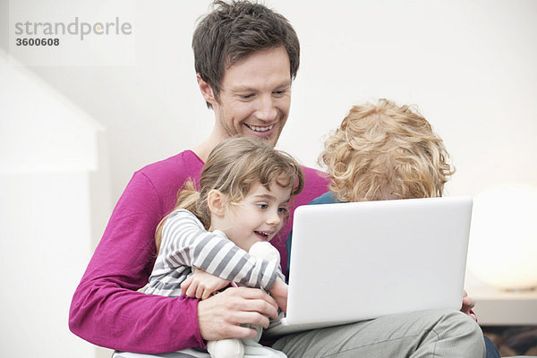 Nahaufnahme eines Mannes,  der seinem Sohn und seiner Tochter bei der Benutzung eines Laptops hilft.
