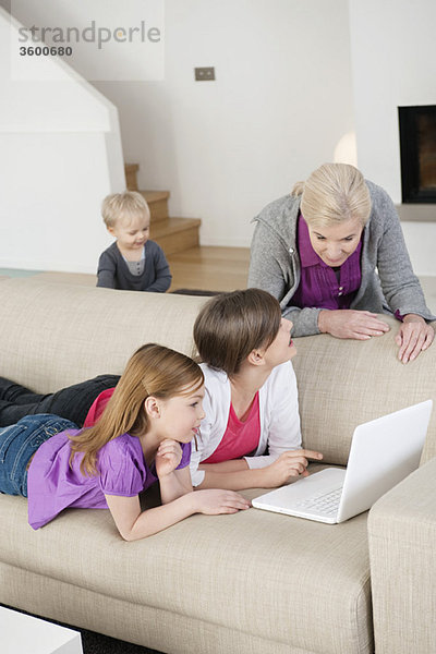 Zwei Mädchen,  die mit ihrer Großmutter einen Laptop auf einer Couch benutzen.