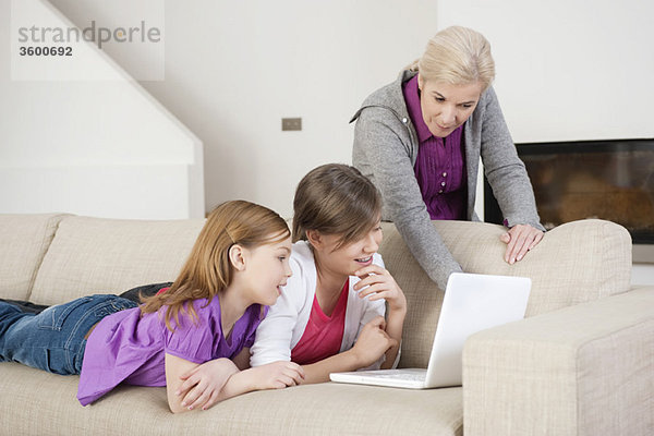 Zwei Mädchen,  die mit ihrer Großmutter einen Laptop auf einer Couch benutzen.