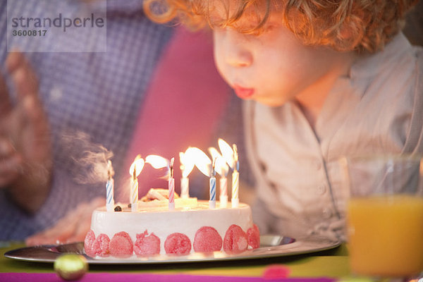Junge,  der Kerzen auf seinem Geburtstagskuchen ausbläst.
