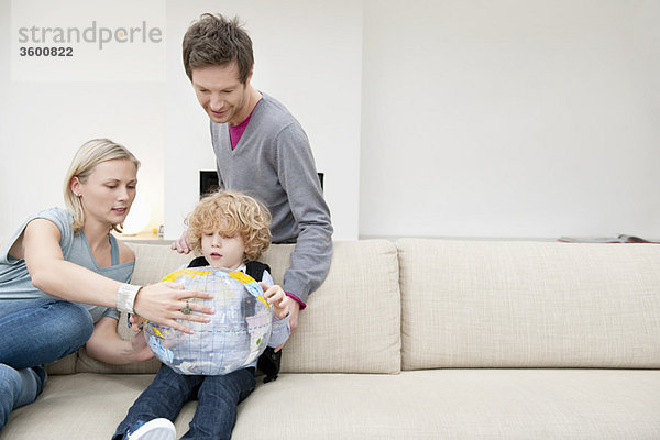 Eltern im Wohnzimmer mit ihrem Sohn,  der einen Globus hält