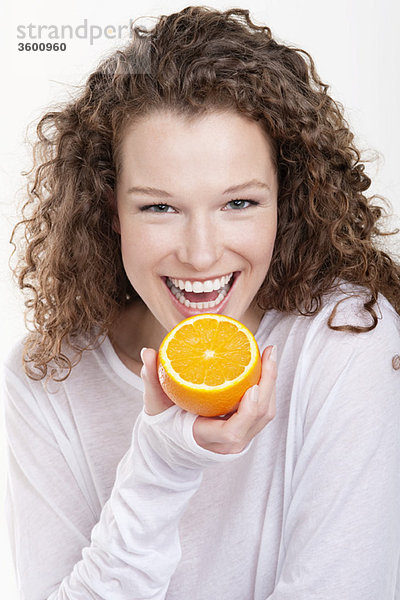 Porträt einer Frau,  die eine halbe Orange hält und lacht