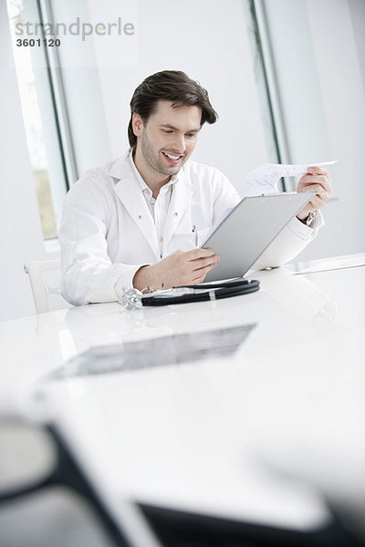 Ein männlicher Arzt,  der einen medizinischen Bericht untersucht und lächelt.