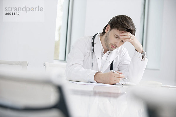 Ein männlicher Arzt sitzt in seinem Büro und sieht verärgert aus.