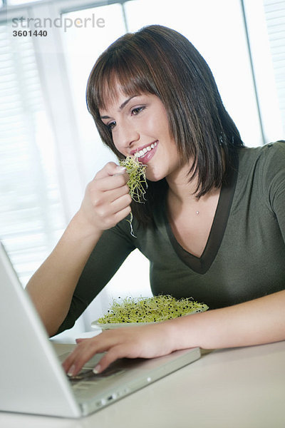 Geschäftsfrau,  die Bohnensprossen isst und einen Laptop benutzt.
