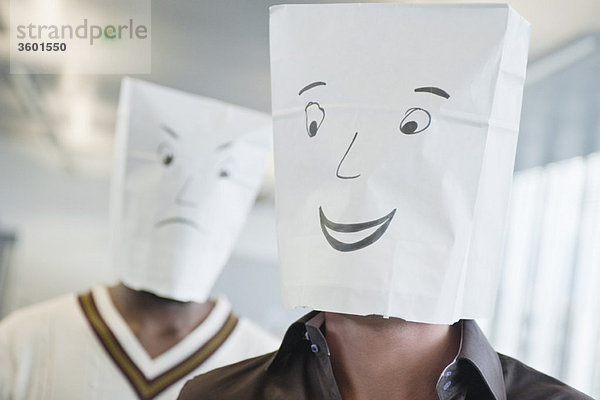 Zwei Geschäftsleute,  die Papiertüten mit fröhlichen und traurigen Gesichtern tragen.