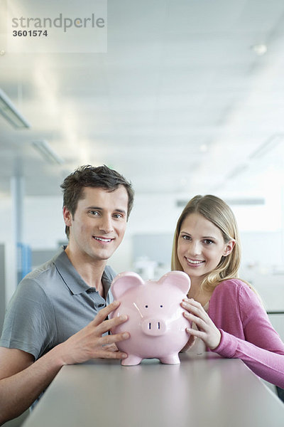 Geschäftsleute,  die ein Sparschwein halten und lächeln