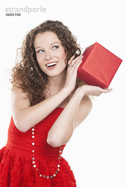 Frau hält ein Geschenk in der Nähe ihres Ohres