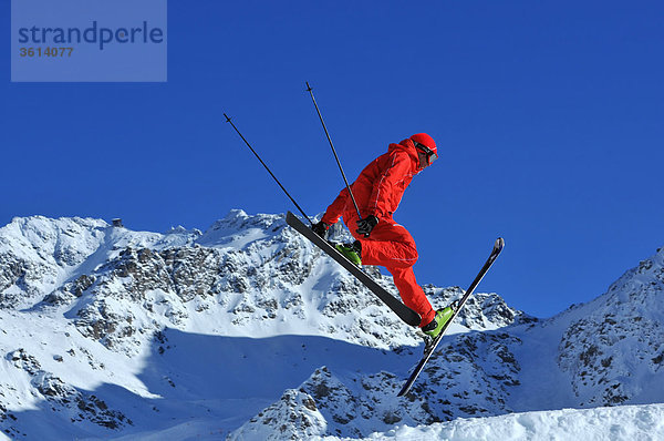 ein Ski Freerider im red-Outfit führt einen Sprung mit gespreizten Beinen
