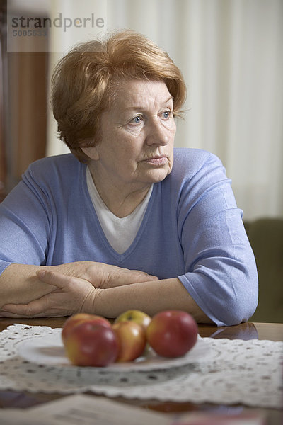 Eine ältere Frau,  die an einem Tisch sitzt und traurig aussieht.