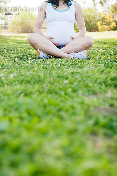 Schwangere junge Frau sitzend im Kreuzbein auf Gras