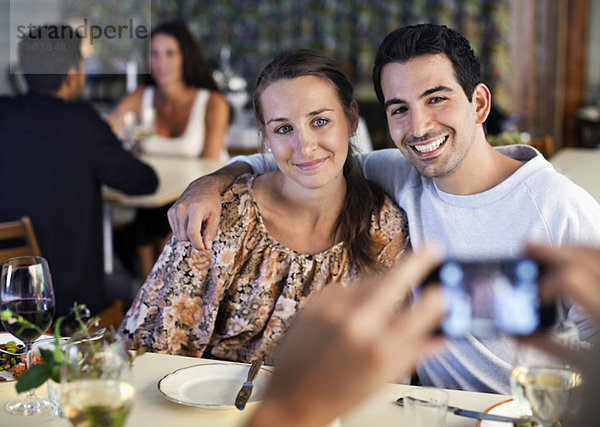Glückliche junge Freunde,  die am Restauranttisch mit Menschen im Hintergrund fotografieren.