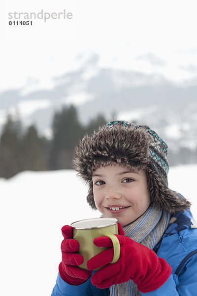 Porträt eines lächelnden Jungen beim Trinken von heißer Schokolade im Schneefeld