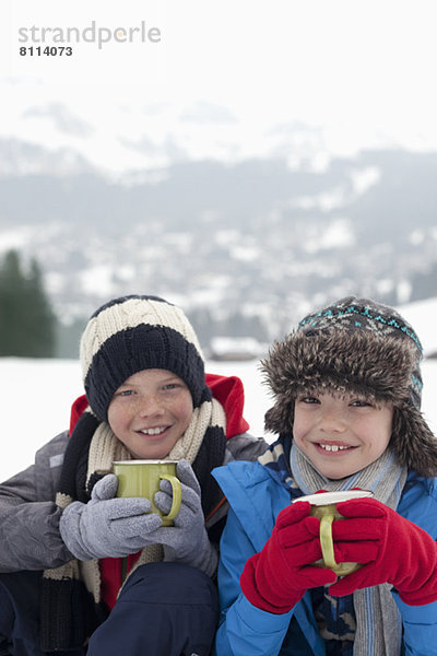 Porträt von lächelnden Jungen beim Trinken von heißer Schokolade im Schneefeld