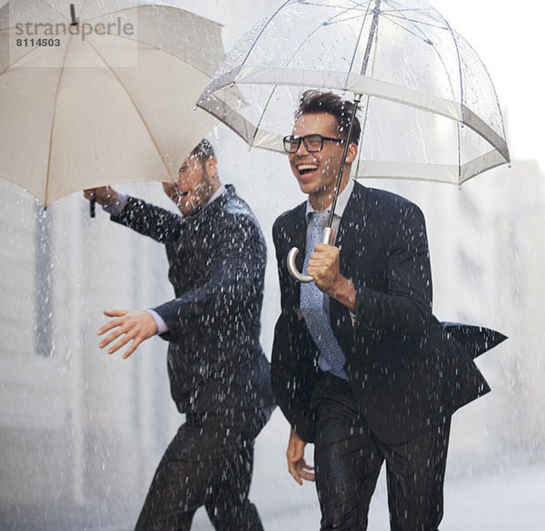 Glückliche Geschäftsleute mit Regenschirmen,  die im Regen spazieren gehen