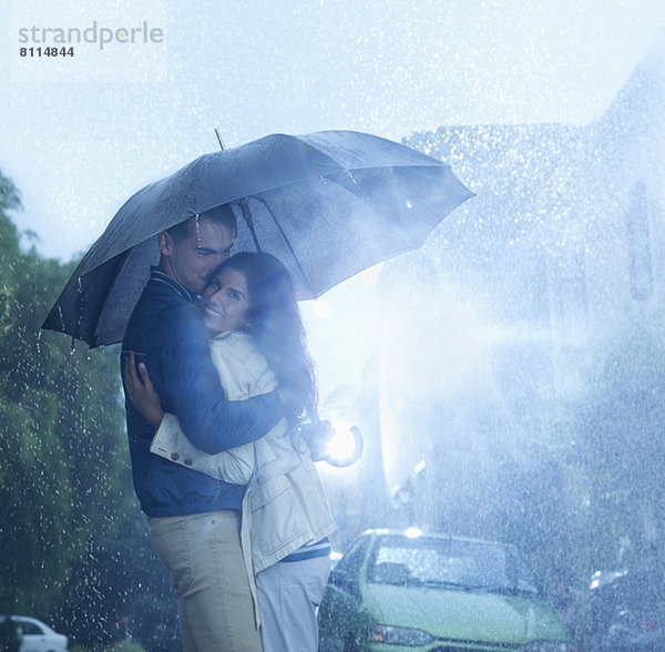 Glückliches Paar,  das sich unter dem Regenschirm umarmt.