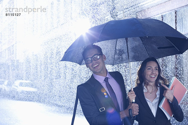 Glücklicher Geschäftsmann und Geschäftsfrau,  die im Regen unter einem Regenschirm spazieren gehen.