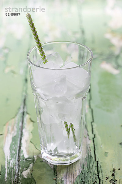 Glas Eiswürfel mit Trinkhalm auf Holztisch, Nahaufnahme