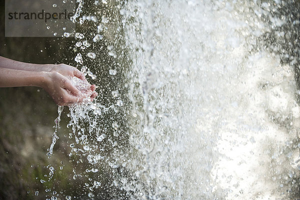 Kind hält Hände unter Wasserfall,  abgeschnitten