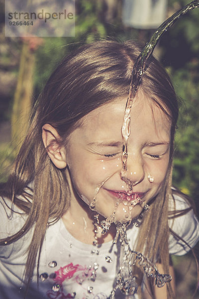 Kleines Mädchen,  das sein Gesicht mit einem Wasserstrahl erfrischt.
