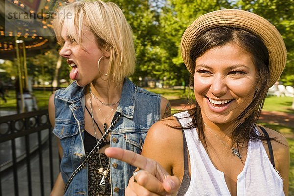 Zwei junge Frauen,  die im Park die Zunge zeigen und herausstrecken.