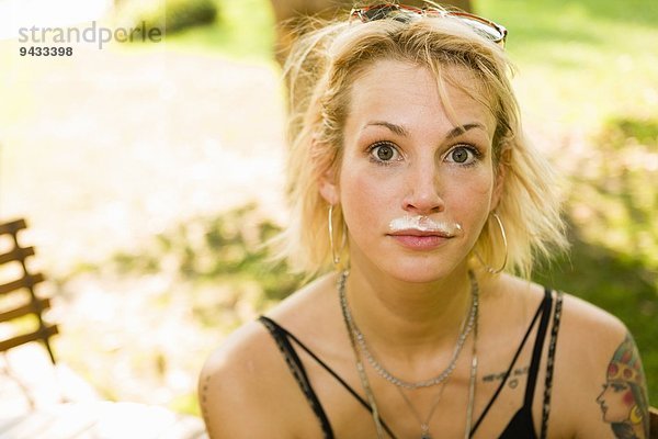 Porträt einer jungen Frau im Park mit Kaffee-Schnurrbart
