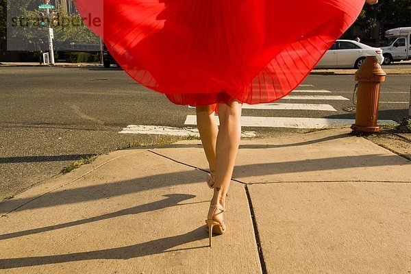 Taille unten Aufnahme einer jungen Frau,  die den Bürgersteig entlang schlendert und einen roten Rock trägt.