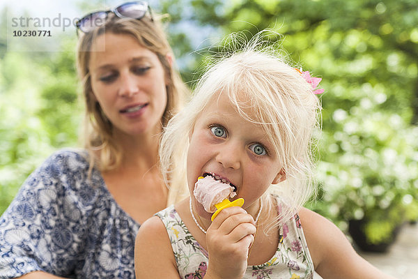 Mädchen beim Eis essen mit Mutter im Hintergrund