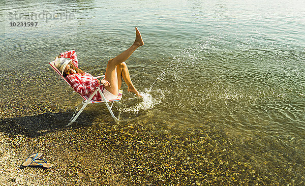 Junge Frau sitzt auf einem Liegestuhl im Fluss und spritzt mit Wasser.