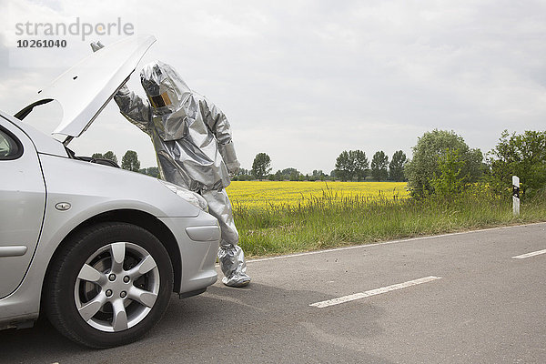 Eine Person in einem Strahlenschutzanzug,  die unter die Motorhaube eines Autos schaut.