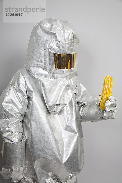 Eine Person in einem Strahlenschutzanzug,  die einen Maiskolben hält.