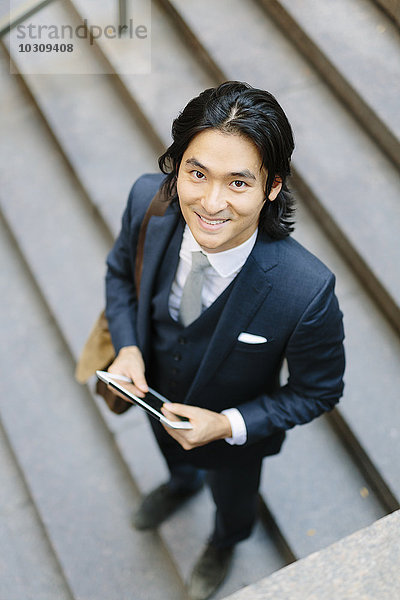 Lächelnder Geschäftsmann steht auf einer Treppe und hält ein digitales Tablett.