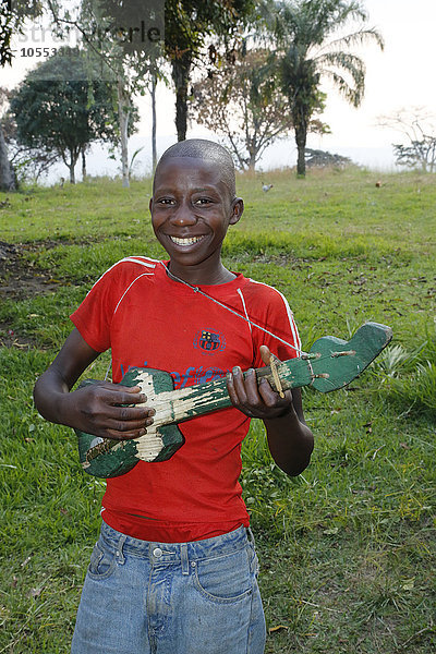 Lachender,  fröhlicher Junge musiziert,  spielt auf selbst gebauter Gitarre,  Matamba-Solo,  Provinz Bandundu,  Republik Kongo