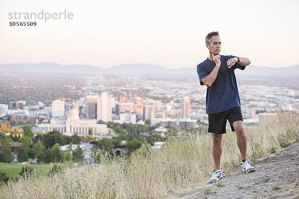 Gemischtrassiger Mann prüft den Puls auf einem Hügel über Salt Lake City,  Utah,  Vereinigte Staaten