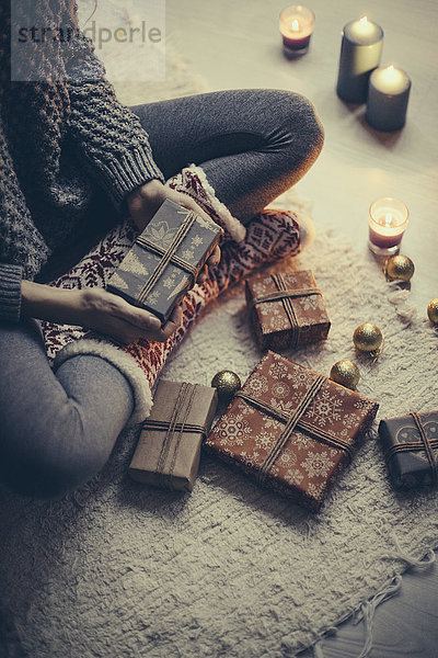 Frau sitzt mit Weihnachtsgeschenken auf dem Teppich