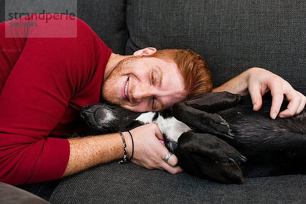 Junger Mann auf dem Sofa liegend umarmend Hundeaugen geschlossen lächelnd