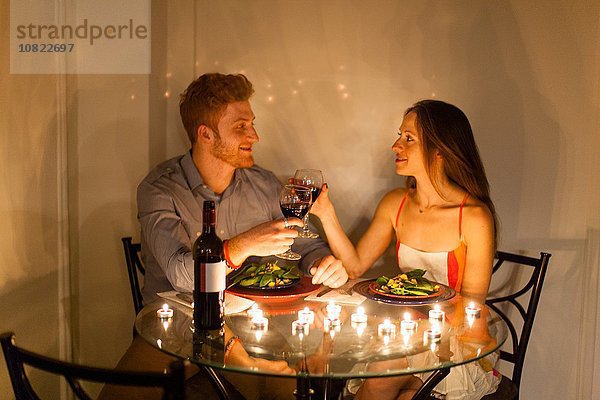 Paar am Tisch von Angesicht zu Angesicht bei Kerzenlicht essen,  einen Toast aussprechen,  lächeln