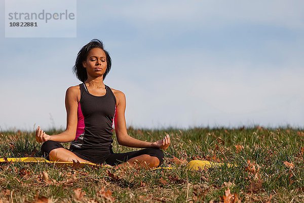 Junge Frau auf Yogamatte sitzend,  im Freien,  in Lotusstellung