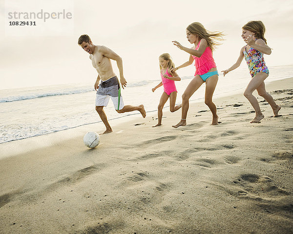 Kaukasischer Vater und Töchter spielen Fußball am Strand