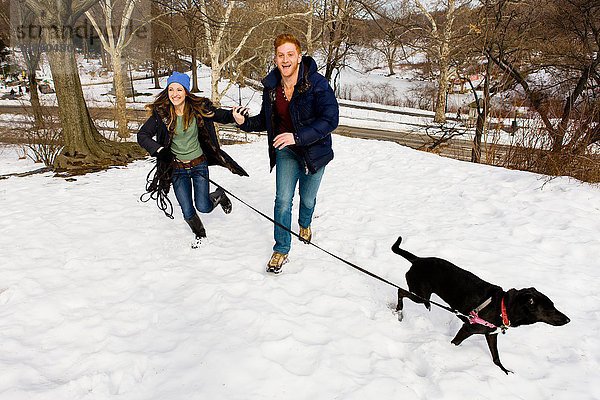 Junges Paar rennt mit Hund im verschneiten Central Park,  New York,  USA