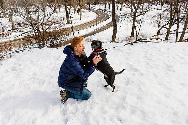 Junger Mann streichelt Hund im verschneiten Central Park,  New York,  USA