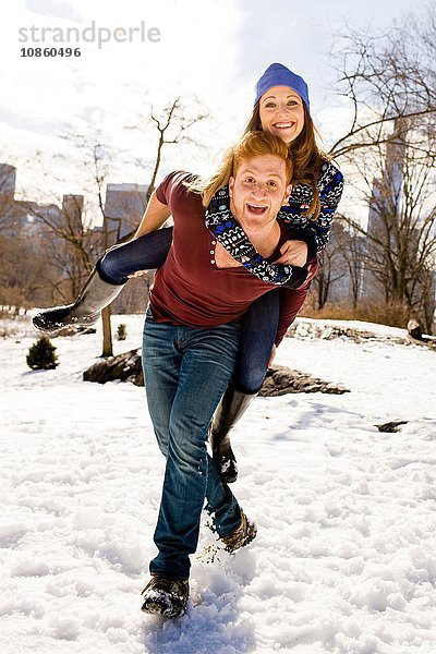 Junger Mann gibt seiner Freundin ein Huckepack im verschneiten Central Park,  New York,  USA