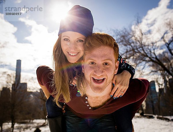 Porträt eines jungen Mannes,  der seiner Freundin im verschneiten Central Park ein Huckepack gibt,  New York,  USA