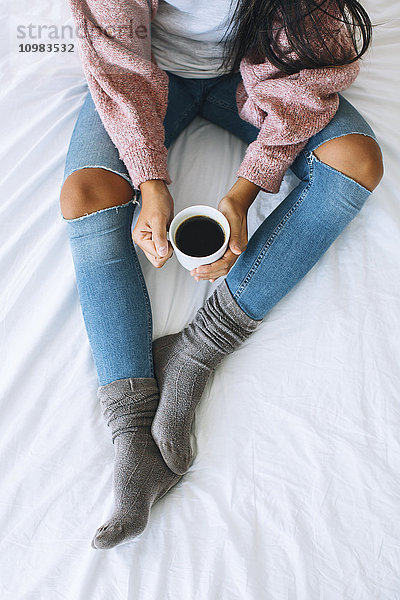 Frau mit Tasse Kaffee auf dem Bett,  Teilansicht