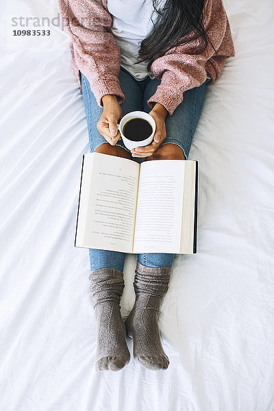 Frau mit Tasse Kaffee und Buch Entspannung auf dem Bett,  Teilansicht