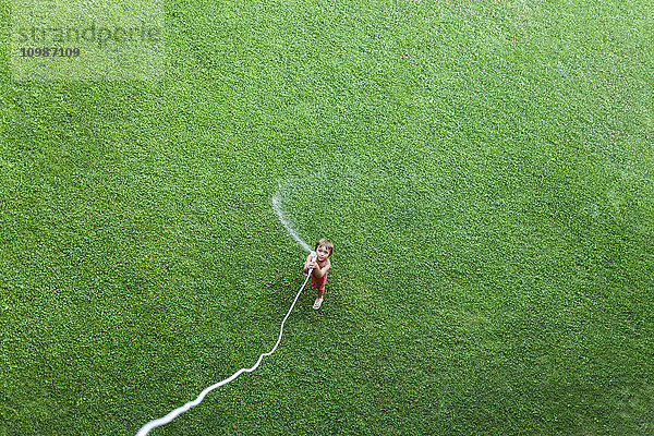 Kleiner Junge auf dem Rasen stehend mit Gartenschlauch,  Draufsicht