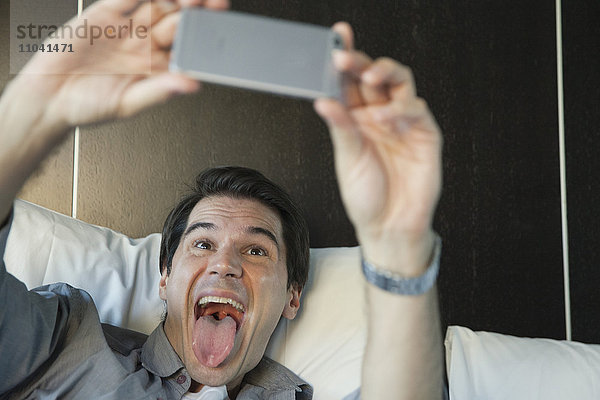 Mann,  der ein Smartphone benutzt,  um einen Selfie zu nehmen,  der die Zunge herausstreckt.